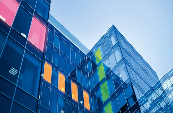 Bürogebäude mit gläserner Fensterfront. Ein Teil der Fenster ist mit LED-Smart-Glas ausgestattet und leuchtet daher rosa, orange oder grün.